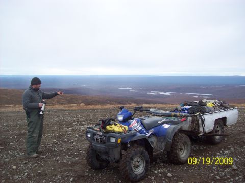 1986 Chevrolet Blazer - A man stands next to a blue ATV and trailer in a vast, open landscape under an overcast sky.