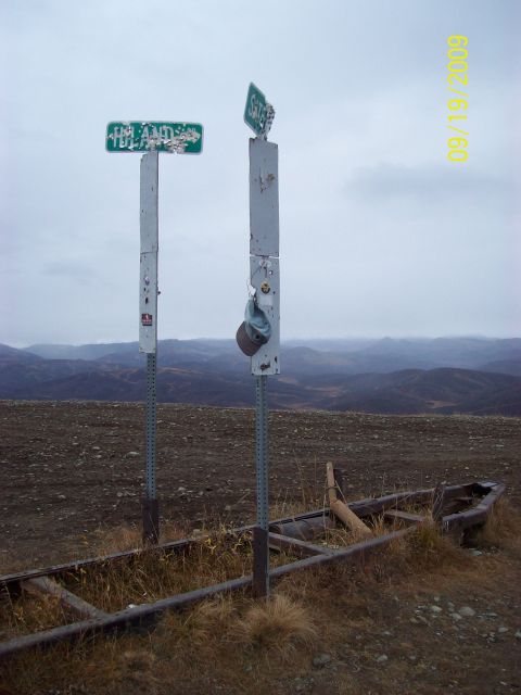 1986 Chevrolet Blazer - A remote location marked by two weathered signposts and the remains of a boat, under a cloudy sky.