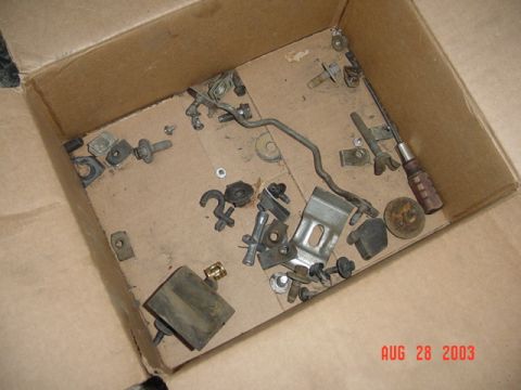 1987 Ford Bronco - Looking down into an open cardboard box holding an assortment of small disassembled vehicle hardware, brackets, clips, bolts, a bent metal…