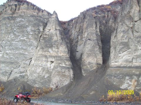 1986 Chevrolet Blazer - A red ATV is parked near a river, with a massive, eroded rock face towering behind it.
