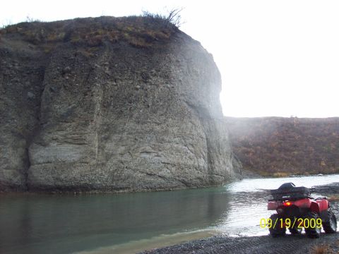 1986 Chevrolet Blazer - A red ATV is parked on a rocky shore beside a body of water, with a large cliff face in the background.