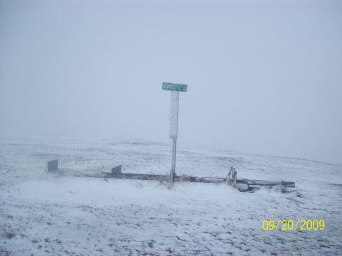 1986 Chevrolet Blazer - A desolate, snow-covered landscape features a weathered signpost and remnants of structures, captured on a winter day.