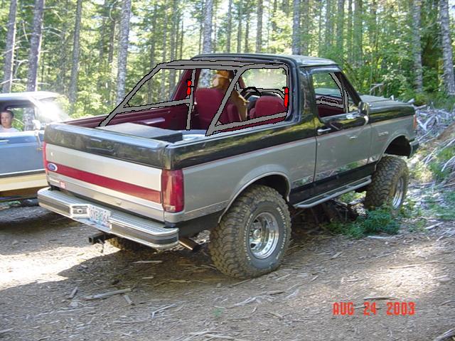 Two-tone gray and black Ford Bronco with a roll cage, seen from the rear