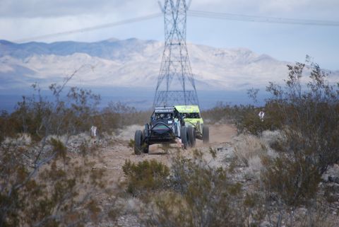 1982 Ford Bronco - Two custom off-road buggies compete on a dusty desert course under a cloudy sky.