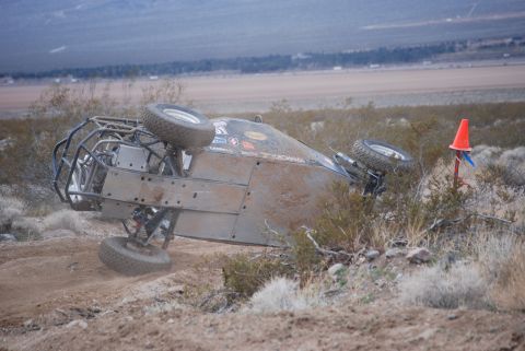 1982 Ford Bronco - An overturned off-road buggy lies on its side amidst desert vegetation, with its tires exposed.