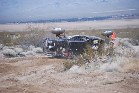 1982 Ford Bronco - Off-road buggy overturned on a dirt track with desert landscape in the background.