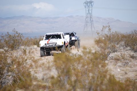 1982 Ford Bronco - Two off-road trucks kick up dust as they compete in a desert race.