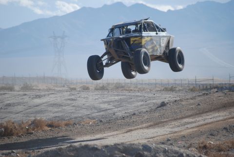 1982 Ford Bronco - A custom off-road buggy soars through the air over a dusty desert landscape.