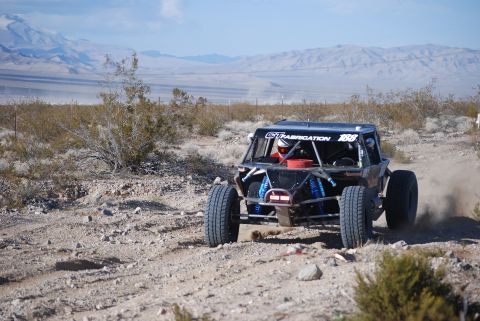 1982 Ford Bronco - An off-road buggy kicks up dust on a desert track, displaying "GT FABRICATION 188" on its side.
