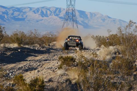 1982 Ford Bronco - A off-road vehicle navigates a dusty desert trail under a clear sky, with mountains and power lines in the background.