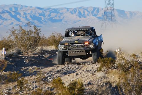 1982 Ford Bronco - This heavily modified truck races through a dusty desert landscape with mountains in the background.