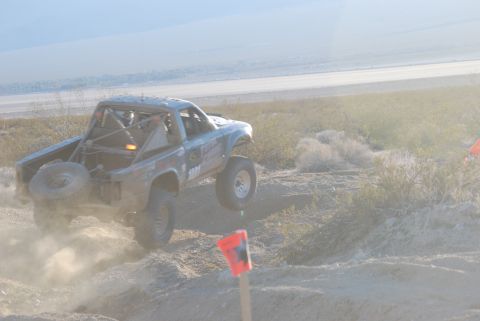 1982 Ford Bronco - A modified off-road truck jumps over terrain, its rear tire visible as it kicks up dust.