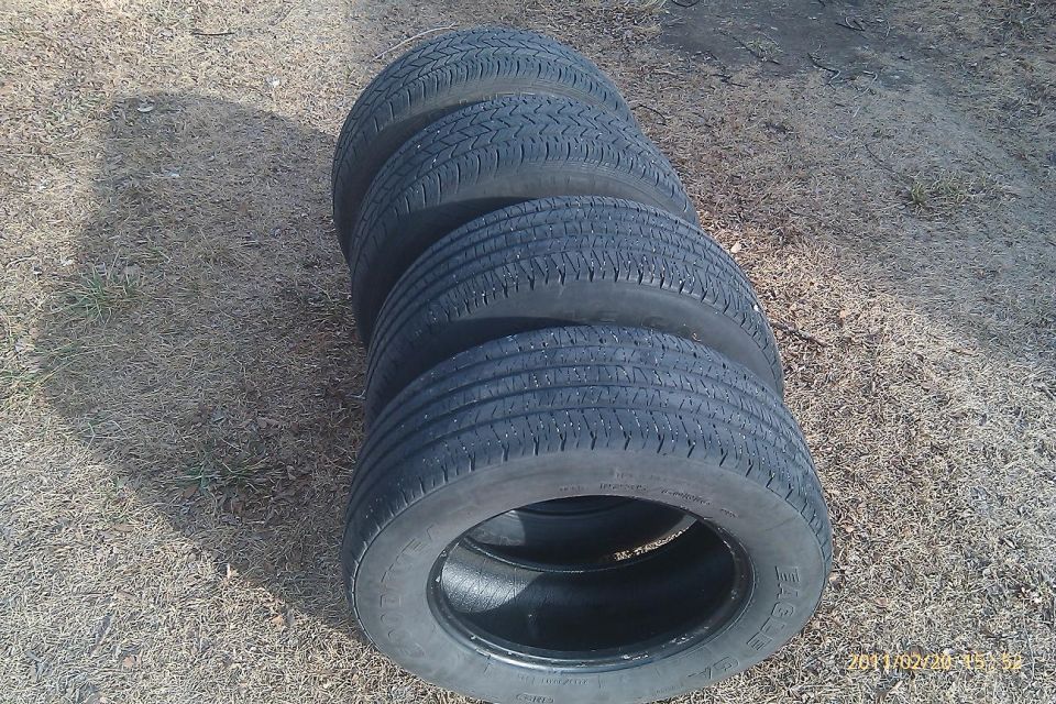 Four used tires stacked on dry ground. One tire is in the foreground, showing its tread and rim