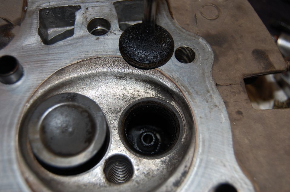 Close-up of carbon-caked valve lifted from cylinder head seat, port and plug hole visible