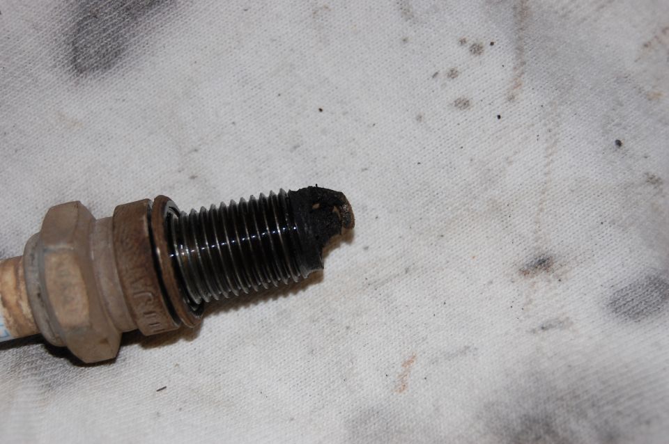 Used spark plug with heavy black carbon fouling on the electrode, on a shop rag