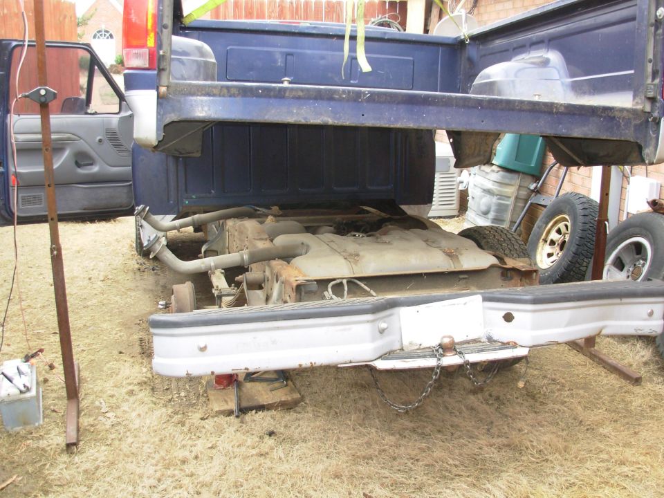 Pickup truck bed raised on stands over its frame in a backyard