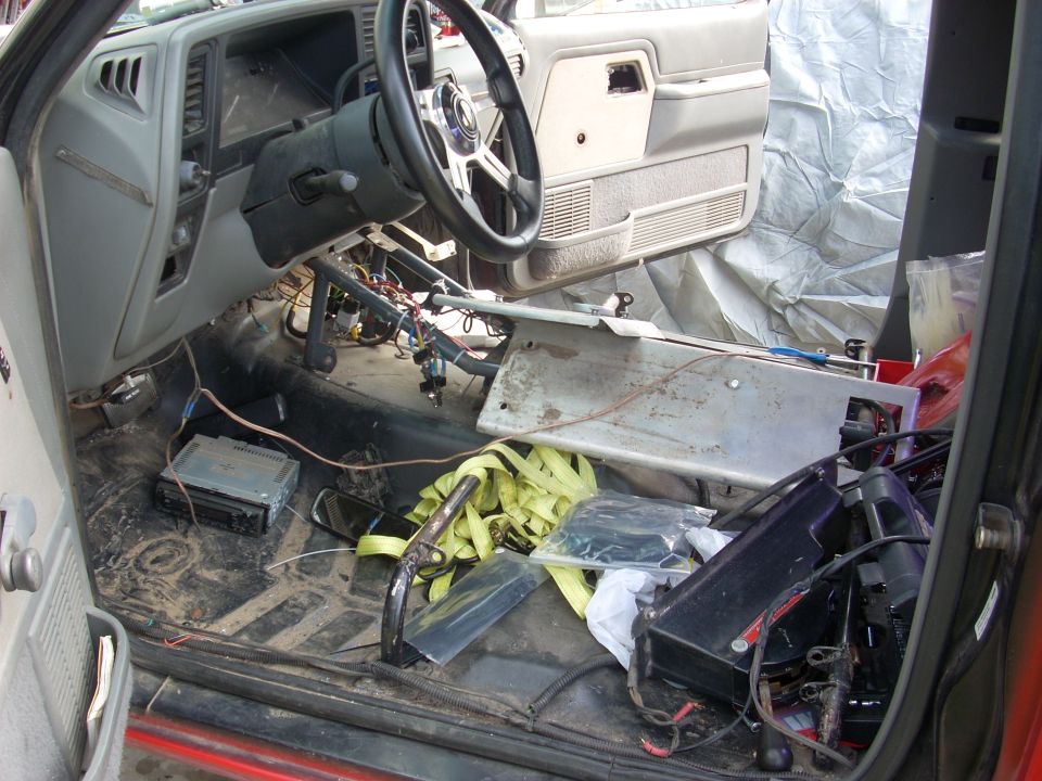 Interior of a vehicle with dashboard removed, exposed wiring, and parts scattered on the floor