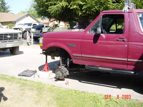 1989 Ford Bronco - 1989 Ford Bronco undergoing maintenance with front wheel removed and vehicle supported by jack stands.
