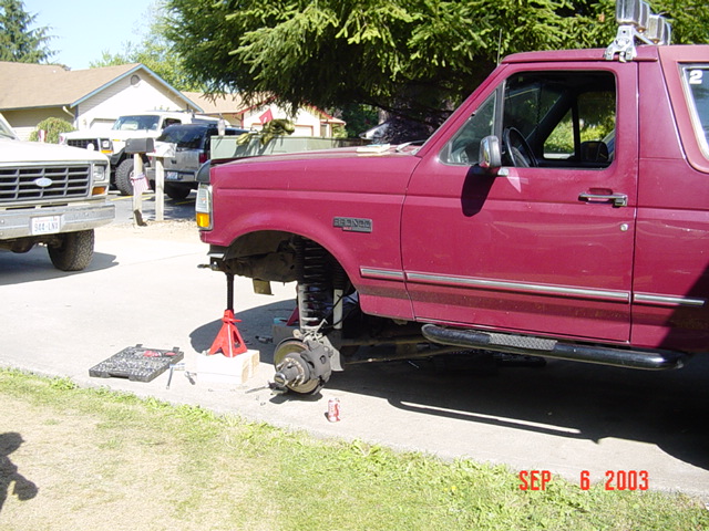 Magenta Ford Bronco on jack stand in driveway with front wheel off, rotor exposed