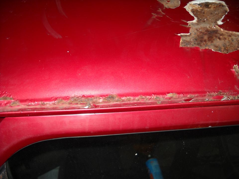 Close-up of red car roof edge with significant rust and peeling paint