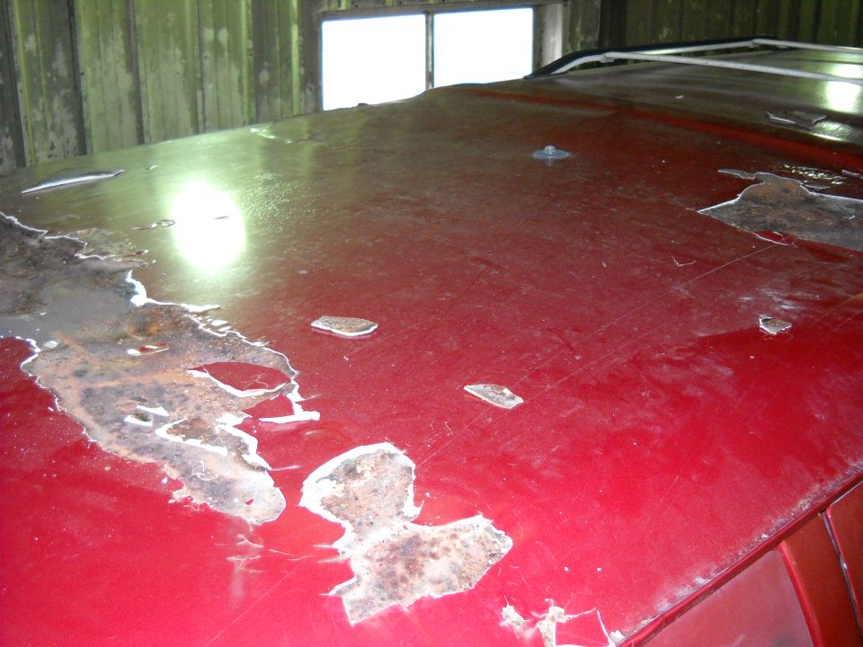 Red vehicle roof with large areas of rust and peeling paint, showing damage and wear
