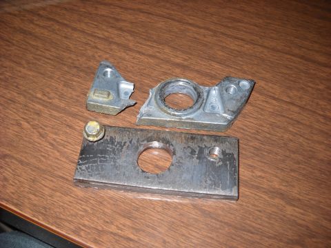 1993 Ford C-150 (Centurion Conversions) - Two broken metal pieces, possibly from a vehicle's armrest mechanism, lie on a wooden table.