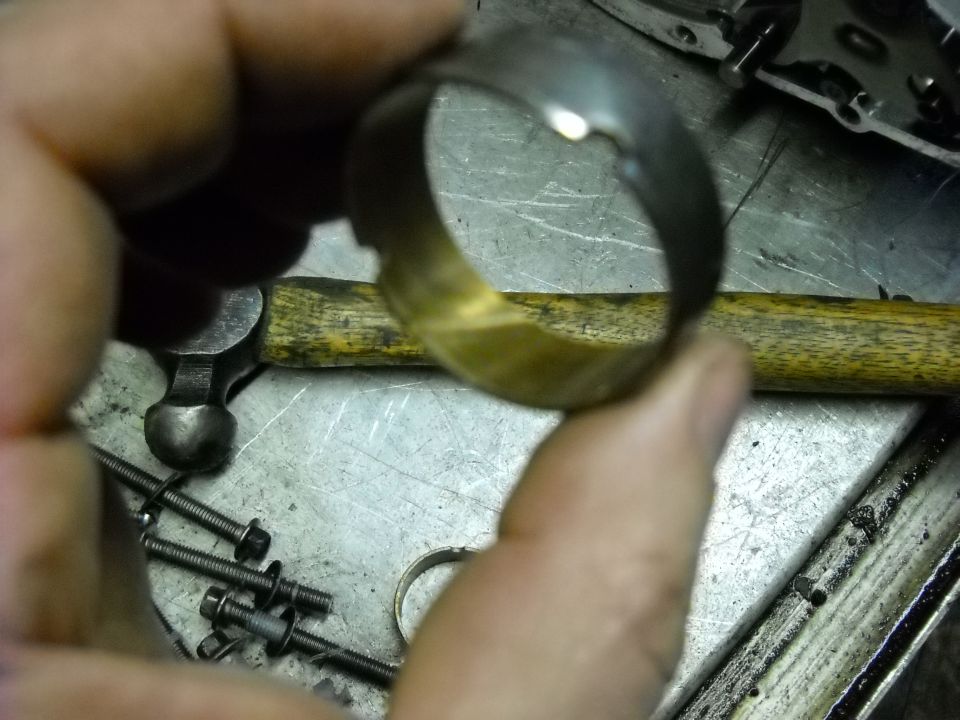 Metal ring with damage held in hand, ball-peen hammer and bolts in background