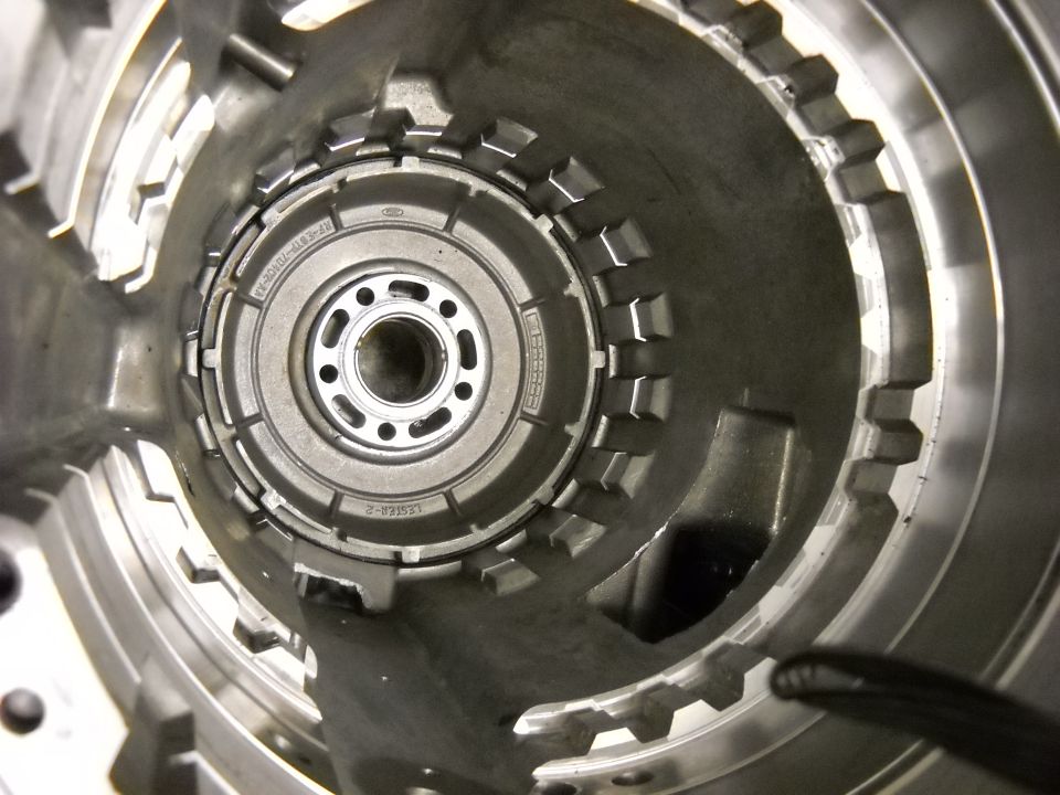Close-up of a transmission torque converter housing with internal gears visible. Part number F81A-10A310-AA is stamped on the housing