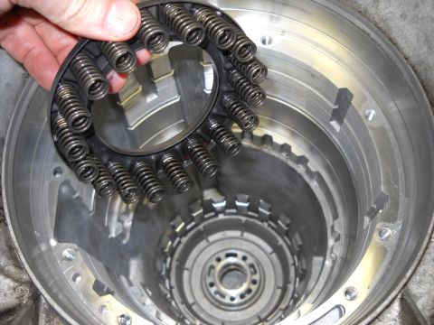 1993 Ford C-150 (Centurion Conversions) - A hand holds a disassembled spring assembly above the internal components of an automatic transmission.