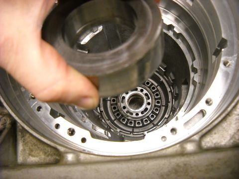 1993 Ford C-150 (Centurion Conversions) - A hand holds a metal ring over the internal workings of a transmission during assembly or repair.