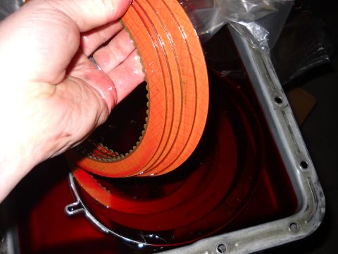 1993 Ford C-150 (Centurion Conversions) - Transmission clutch plates are held over a pan of fluid, indicating a part replacement or inspection.