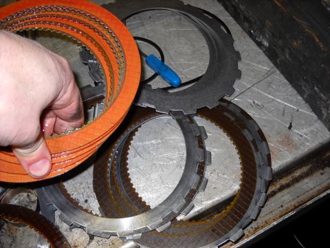 1993 Ford C-150 (Centurion Conversions) - A hand holds a stack of orange transmission clutch plates next to steel plates on a metal surface.