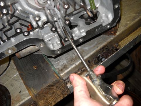 1993 Ford C-150 (Centurion Conversions) - Close-up of a transmission case during a rebuild, with a tool being used to access internal components.