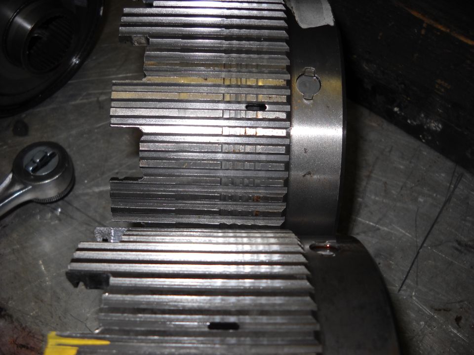 Close-up of a transmission clutch pack with visible wear and damage. A ratchet is nearby