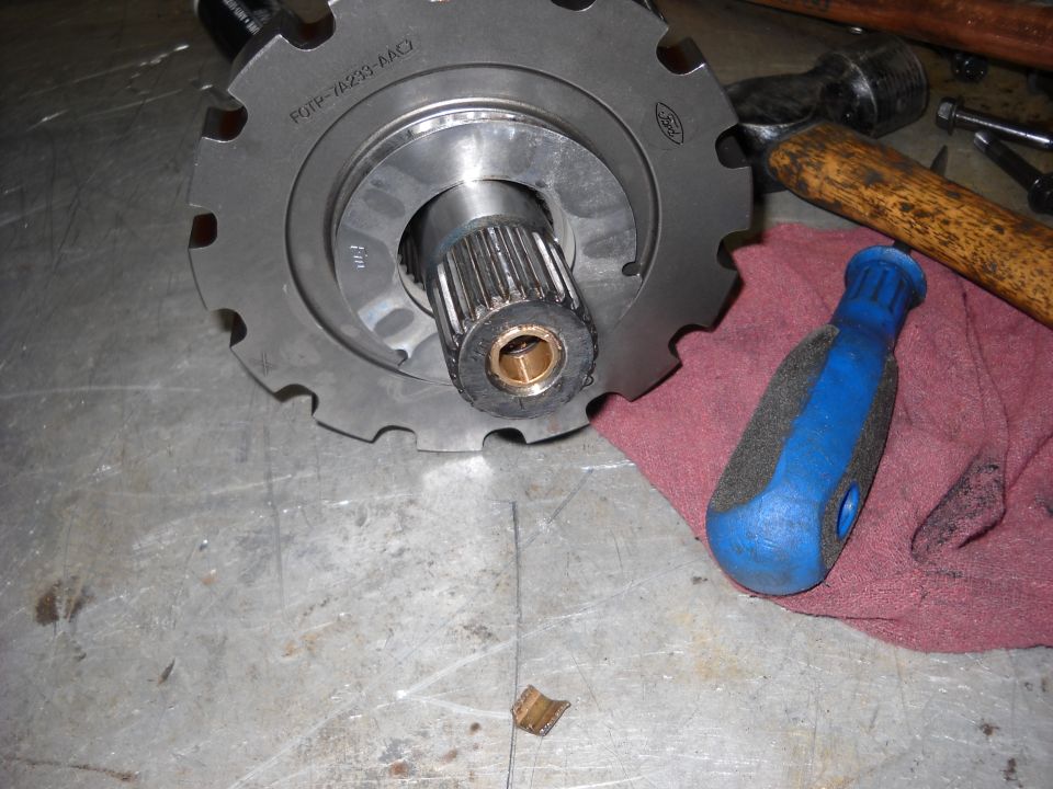 Close-up of a transmission part with splines and a gear, resting on a metal surface next to a screwdriver and hammer