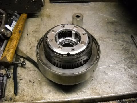 1993 Ford C-150 (Centurion Conversions) - A disassembled transmission component sits on a metal workbench next to a hammer and pliers.