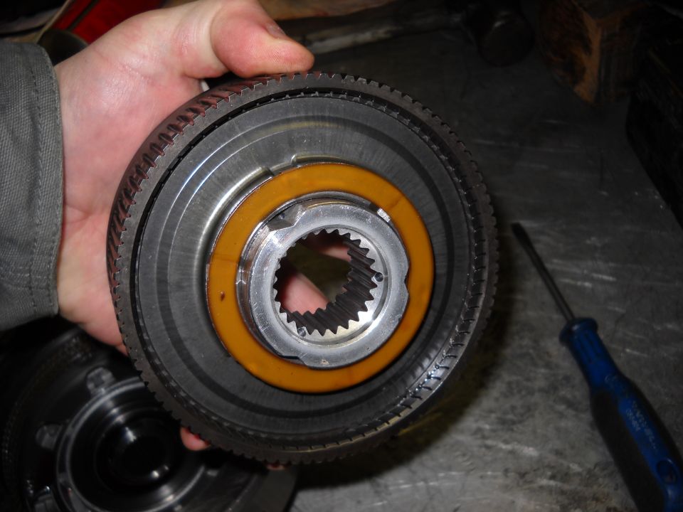 Close-up of a metal transmission component with splines and an orange ring, held by a hand