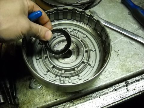 1993 Ford C-150 (Centurion Conversions) - Mechanic's hand holding a seal over a disassembled automatic transmission drum, revealing internal components.