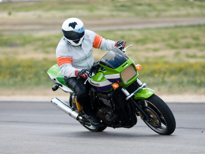2001 Kawasaki KZ1000-A1 - A rider in a white helmet and jacket with orange stripes leans into a turn on a green Kawasaki motorcycle.