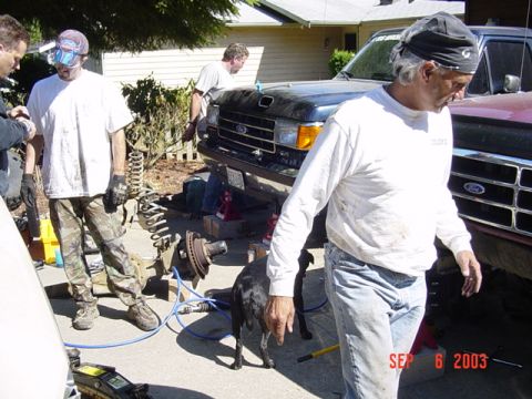1989 Ford Bronco - Two Ford trucks, one dark blue and one maroon, are parked outside a house with people working on the front of the blue truck.