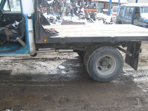 1972 Ford F-250 - This 1972 Ford F-250 flatbed truck is seen from the side in a yard with other vehicles and parts.