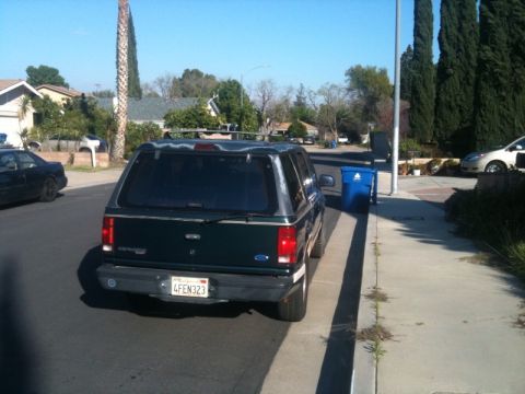 1993 Ford Taurus - Dark green SUV with camper shell parked on street, showing rear view and license plate.