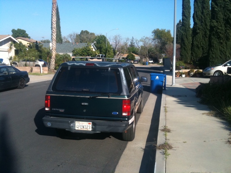 Rear view of a dark green SUV with a camper shell parked on a residential street. License plate reads 4FEN323