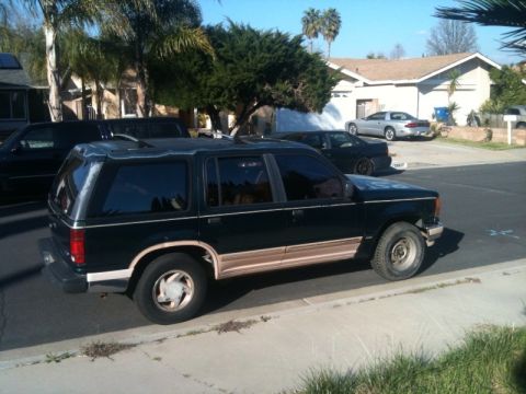 1993 Ford Taurus - A dark green SUV with tan trim is parked on the side of a residential street.