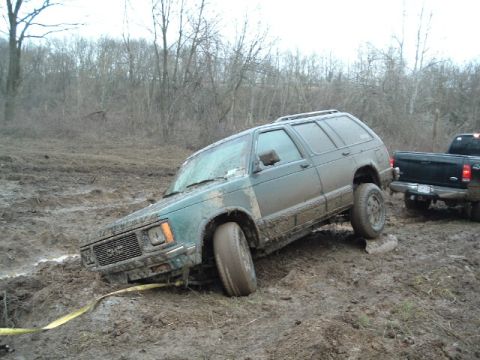 1993 Ford Bronco - A green SUV is stuck in thick mud, with a black pickup truck nearby.