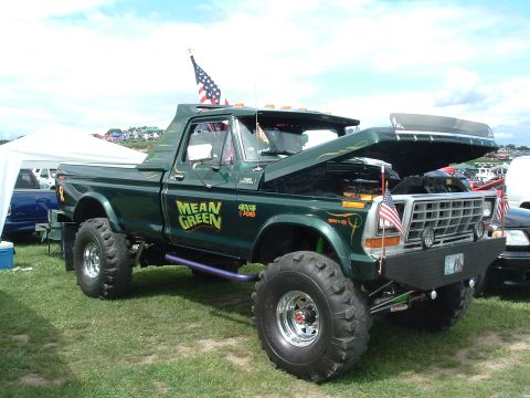 1993 Ford Bronco - This lifted green pickup truck, identified as a 1979 Ford F-150, features custom "MEAN GREEN" graphics and an American flag on its antenna.