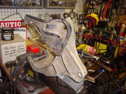 1989 Ford Bronco - A metal bracket is clamped in a vise on a workbench cluttered with tools and automotive parts.