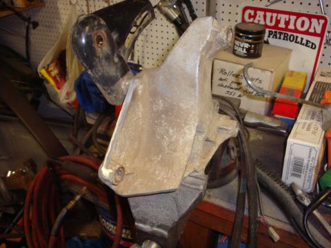 1989 Ford Bronco - An alternator bracket is secured in a vise, with various automotive parts and a warning sign visible.