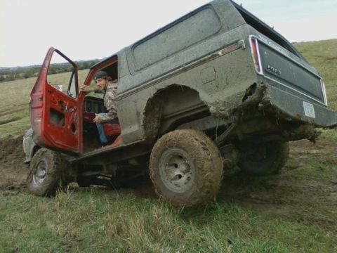 1978 Ford Bronco - A muddy 1978 Ford Bronco is stuck in the mud, its driver's door open with a person sitting inside.
