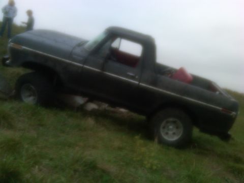 1978 Ford Bronco - A dark pickup truck with a red interior is parked on a grassy incline.
